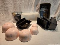 Group shot showing all bakeware items: Calphalon loaf pan in packaging, Glasbake loaf pan, mini loaf pans, tart pans in package, pink melamine bowls