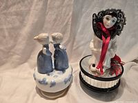 Both porcelain music boxes side by side showing figurine details and bases