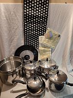 Entire cookware set with lids, steamer insert, apron, tea towel and pot holder visible