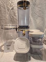 All eight storage containers arranged: five OXO POP minis, two smoky blue latch canisters stacked, one clear ribbed Oggi jar