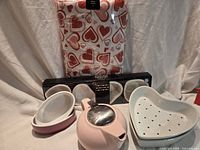 Group shot showing tablecloth package, boxed ramekins, oval bakers, heart strainer, teapot