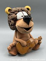 Full view of seated clay lion piggy bank with guitar