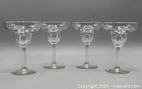 Four clear glass margarita glasses lined up side by side on neutral background