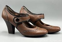 Side view of both pumps showing strap, wingtip detailing, heel height