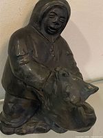Front angle of dark cast sculpture showing Inuit man crouched with wolf
