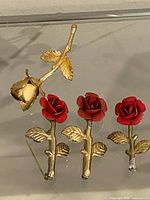 Front view showing three red enamel rose brooches and one gold-tone rose bud brooch