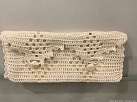 Front view of crocheted off-white clutch showing lattice pattern and rosettes