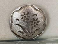 front view of circular silver-tone openwork brooch with floral cut-out