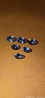 Six loose oval blue tanzanite gems on textured surface