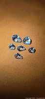 Six light blue faceted aquamarines on brown background