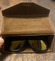 Sunglasses seated in open brown case, front view