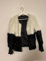 Front view of black and white faux fur jacket on hanger