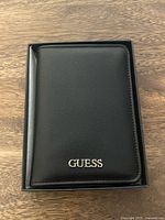 Front view of black Guess leather wallet in box showing logo