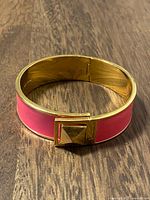 Closed pink enamel gold-tone bracelet on wood surface