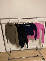 Four Lululemon garments on rack: olive hoodie, black pullover, navy cropped top, pink top