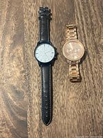 Both watches side by side on wooden surface, showing full straps and bracelets