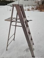 Full side view of folded aluminum A-frame ladder on snow