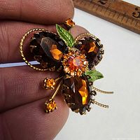 Close-up of gold-tone brooch with amber rhinestones and green enamel leaves next to ruler for scale