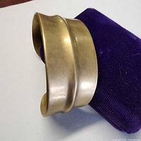 Wide brass cuff bracelet displayed on purple stand
