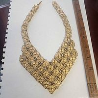 Full view of gold-tone bib necklace beside ruler for scale