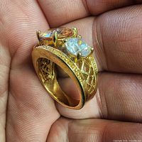 Gold-tone ring held in hand showing three stones and lattice shank