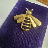 Front view of gold-tone bee brooch on velvet pad