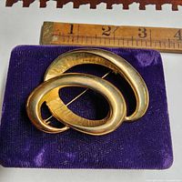 Front view showing gold-tone brooch on velvet pad with ruler for scale