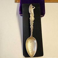 Full view of ornate sterling silver souvenir spoon on black backing