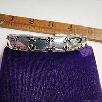 Full view of silver-tone floral cuff bracelet beside ruler