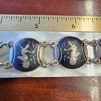 Close-up of two niello panels showing dancer motif and sterling links next to ruler for scale