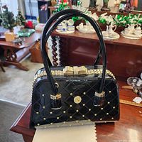 Full view of Susen black quilted handbag showing studs, handles and bow detail