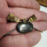 Close-up of brooch showing curling stone engraved "GLENMORE - J.T." and two crossed brooms