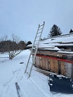 Full view of aluminum ladder leaning against roof in snow
