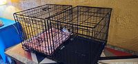 Both black wire pet crates side by side on table, showing trays and interior