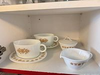 Two handled soup cups on matching saucers, sugar bowl with lid, creamer, all showing Butterfly Gold pattern