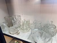 Shelf with assorted clear glassware including vases, bowls, pitcher, relish dish, candlestick, trays