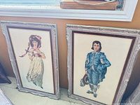 Both framed needlepoints leaning against wall