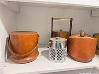 Four ice buckets: leatherette, lattice metal, wood veneer with brass handle, leatherette with brass knob