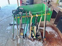 Overall view of assorted shovels, axes/mauls and bow saw leaning against background