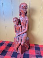 Front view of red plaster sculpture mother and son on check cloth