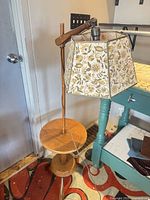 Full view of wooden floor lamp with attached shelf and floral shade