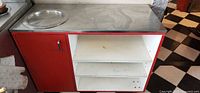 Front view of red prep counter showing stainless top, round insert, cabinet door and shelves