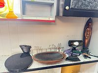 All items arranged on countertop: marble lazy Susan, metal vase, wooden tray, wire sign, cast iron iron, green plow toy, lamp fixture, copper relief plaque