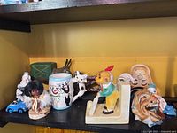 All items grouped on shelf including clown ashtray, boy dispenser, tumbler, dolls, animals, ashtray