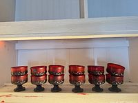 Full set of nine ruby red Franciscan Madeira footed glasses on shelf