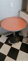 Full view of round red laminate bistro table against wall on checkered floor