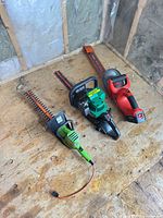 Three hedge trimmers on plywood surface