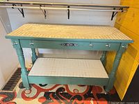 Full view of teal kitchen island showing tile top, drawers, lower shelf, turned legs