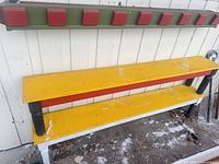 Two benches, one upright (yellow/red/black), one inverted on wall (green/red)