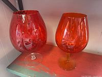 Both red art glass stem vases side by side